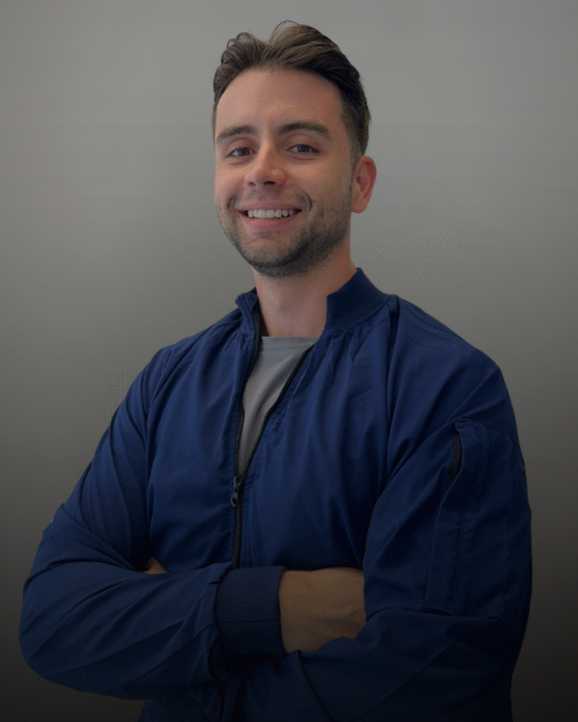 Портрет на усмихнат лекар по дентална медицина с тъмносиня работна униформа, на сив фон.